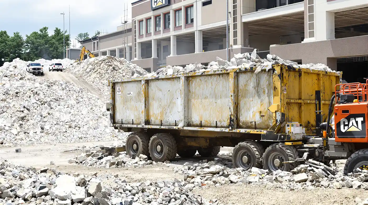 Large roll-off dumpster loaded with broken concrete and demolition debris at an active Kansas City commercial demolition site with crushed concrete piles in the background