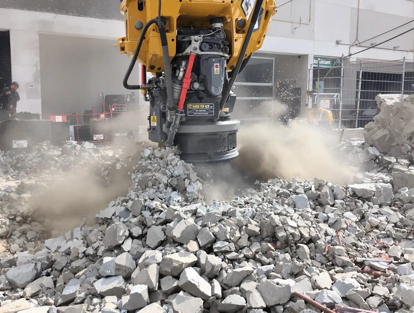 Hydraulic breaker on an excavator demolishing a concrete slab with exposed rebar and dust at a Kansas City site