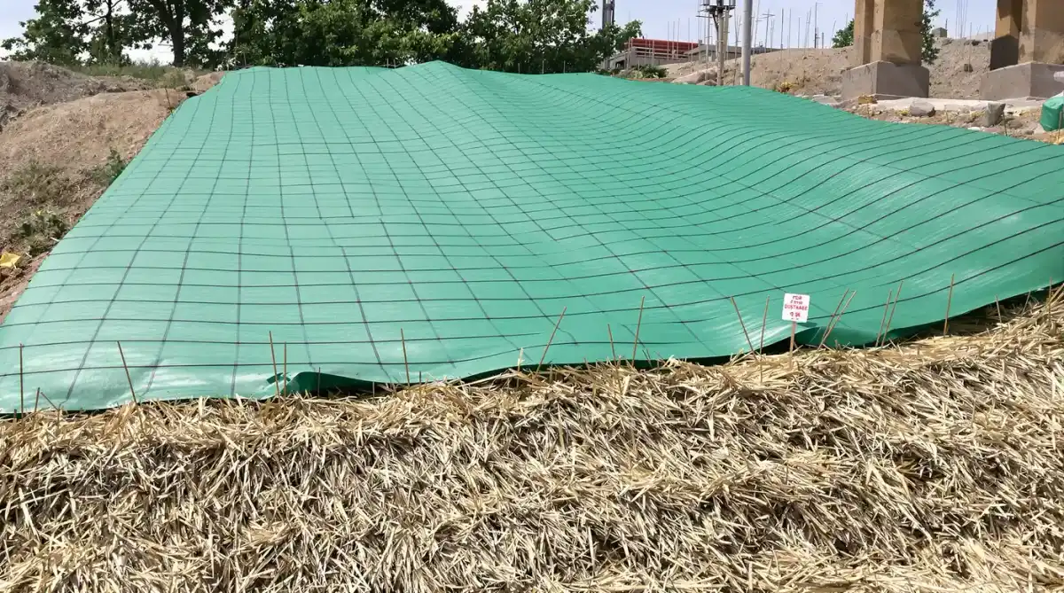 Green erosion control blanket pinned to a graded slope with straw wattles at the toe on a Kansas City construction site