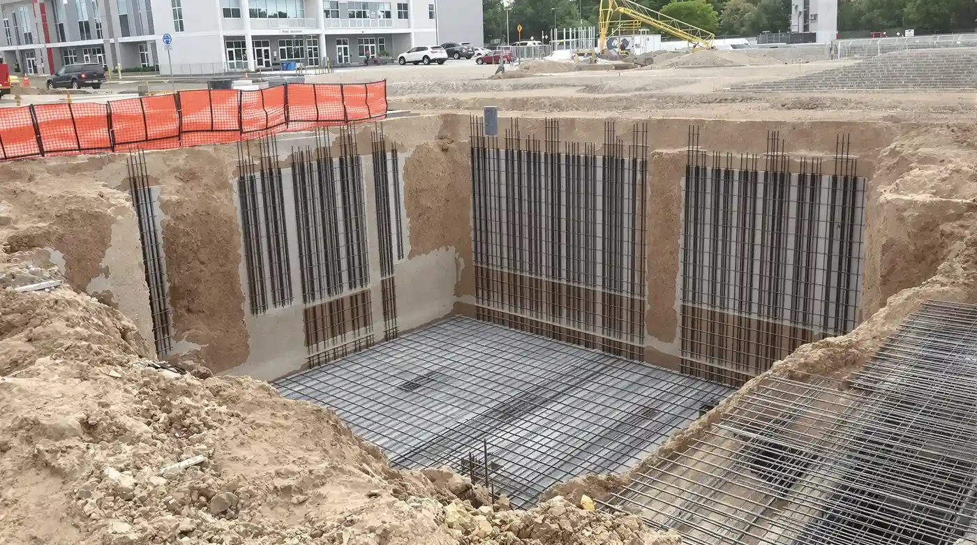 Clean-cut commercial foundation excavation in Kansas City with sharp vertical walls and staged rebar cages ready for concrete pour